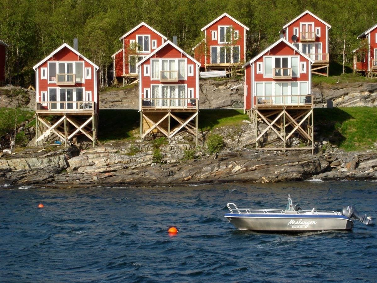 Røde rorbuer på pæle set fra fjorden med en båd foran