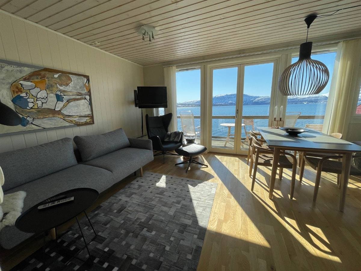 Stue og spiseplads i lejligheden med fjordudsigt gennem altandørene